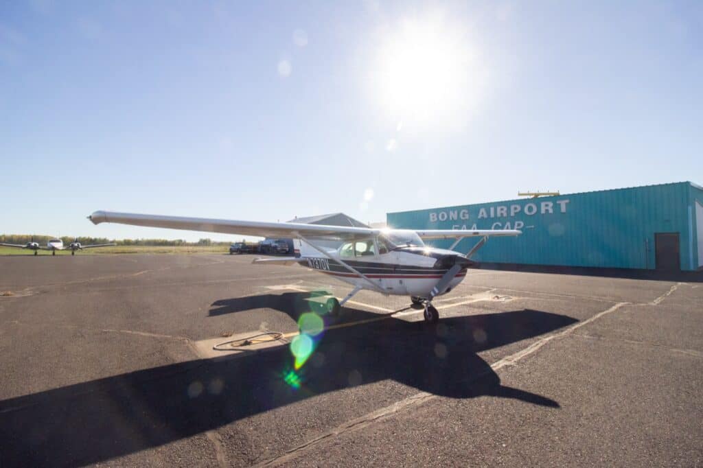 A Cessna 172 parked in front of the Bong Airport hangar at KSUW, into a low sun.