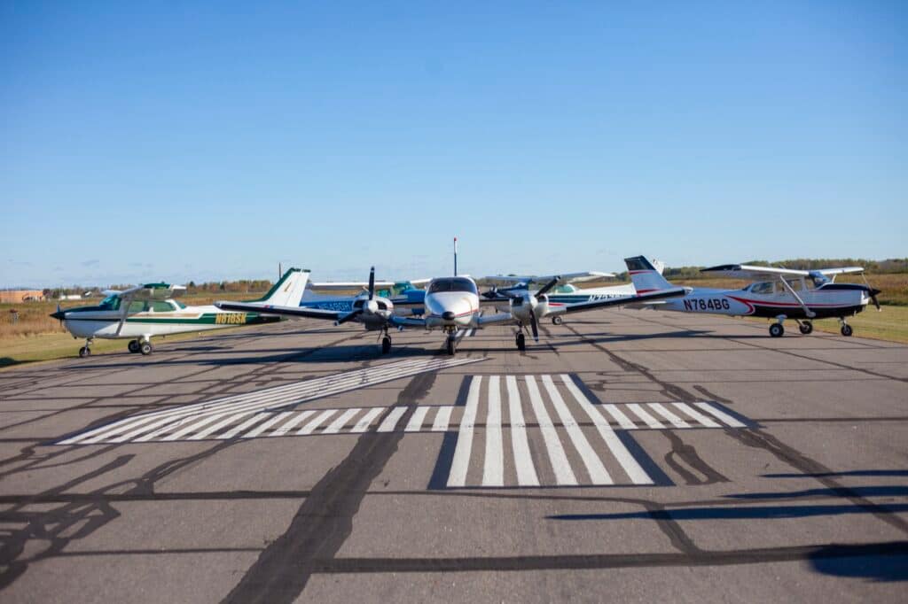 Four aircraft parked nose-on across the hold-short markings at KSUW: the Cessna 172 N616SK, a Cessna 172 in blue, the Piper Seneca, and the Cessna 172 N784BG.
