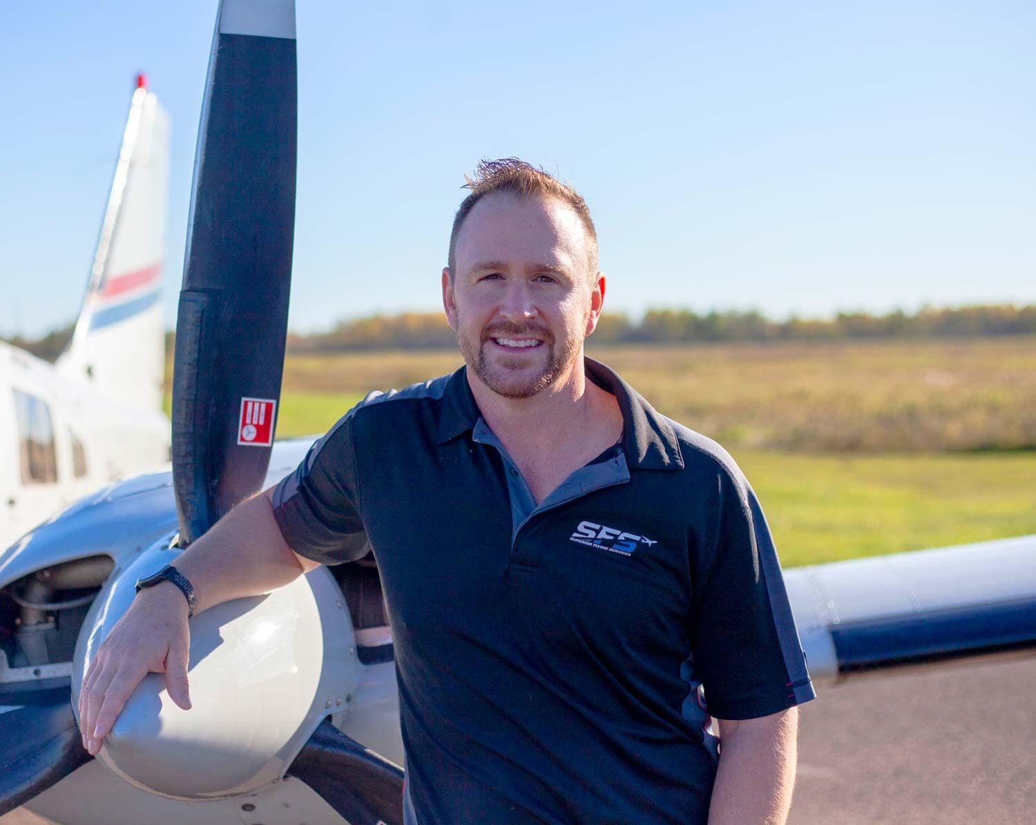 Calvin Kramp standing with his hand on the propeller of the Piper Seneca on the ramp at KSUW.